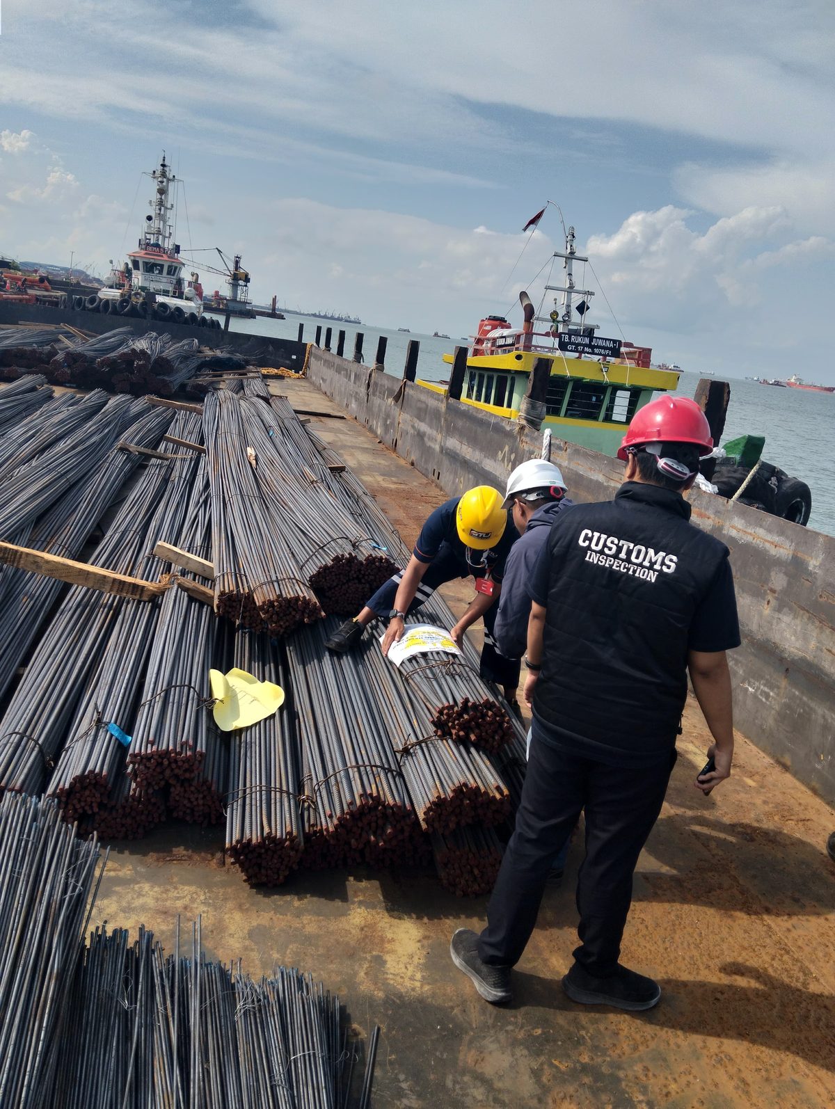 Petugas berhelm memeriksa tumpukan besi beton di atas tongkang