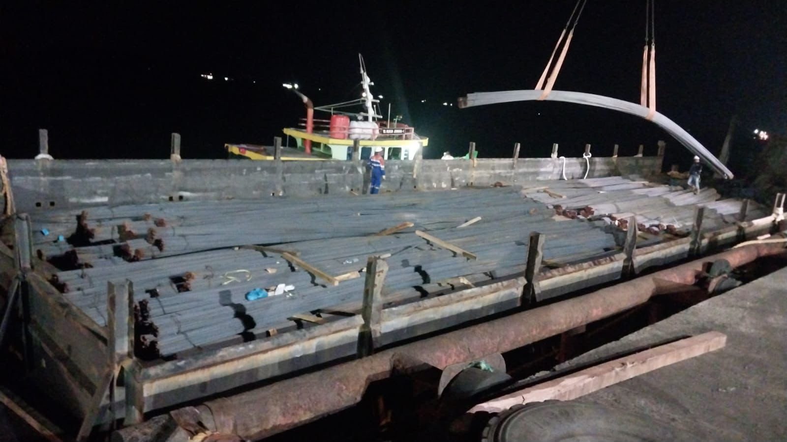 Tongkang dimuati besi beton pada malam hari dengan bantuan crane