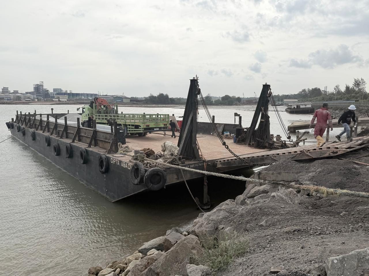 Tongkang bersandar di dermaga dengan truk crane di atas deck